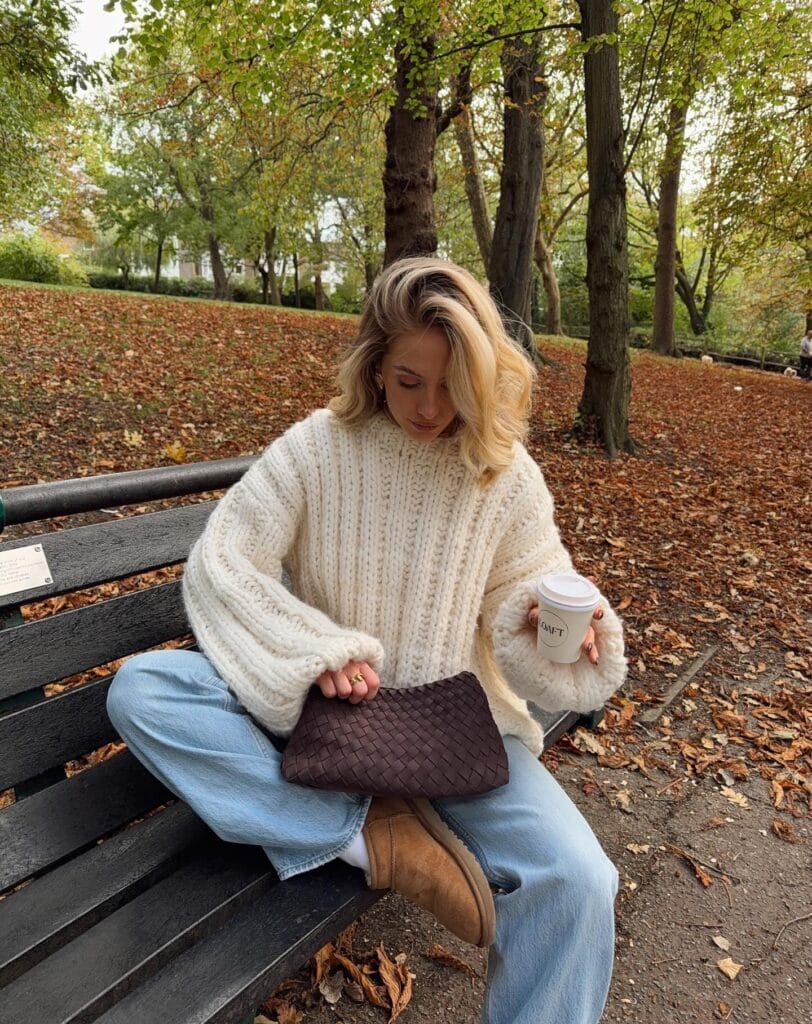 Everyday fall outfit with cream cable-knit sweater, light-wash jeans, tan UGGs, and dark woven bag.

