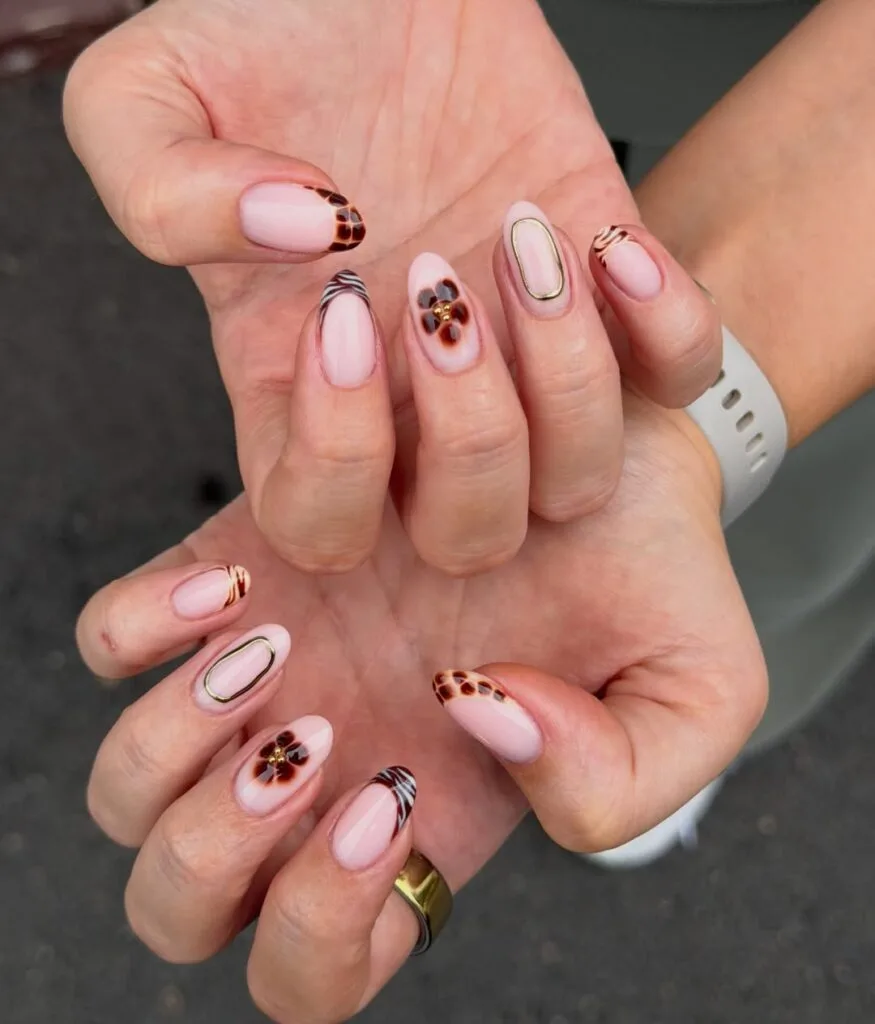 Autumn nails with sheer pink bases, tortoiseshell and zebra tips, blurred brown flowers, and thin gold outline accents
