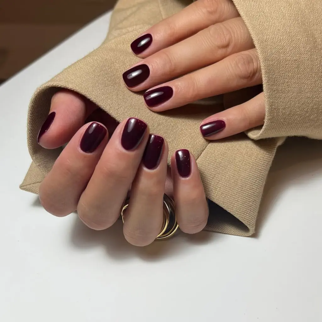 Glossy short fall nails in deep plum berry color with high shine finish and rounded shape