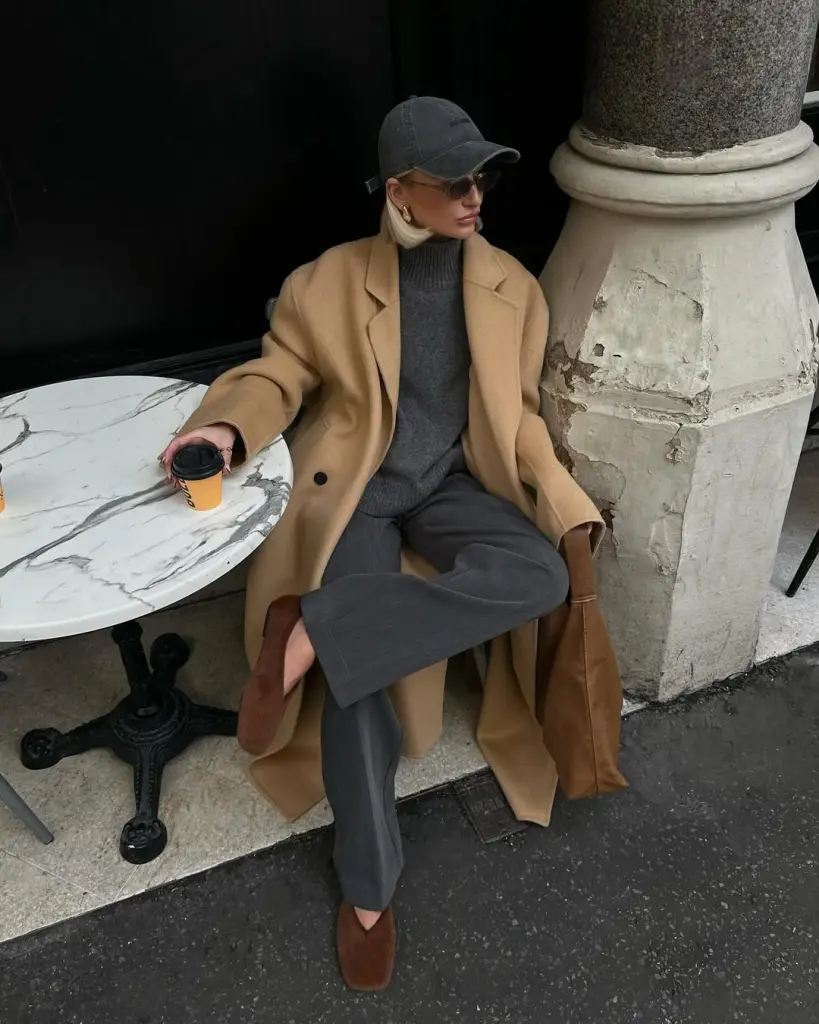 fall outfit with camel wool coat over gray knit sweater and matching gray trousers, styled with brown suede ballet flats and baseball cap