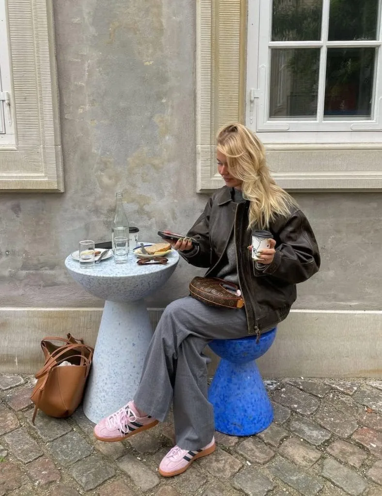 Casual fall outfit with black leather jacket, gray trousers, pink sneakers, brown leather bag
