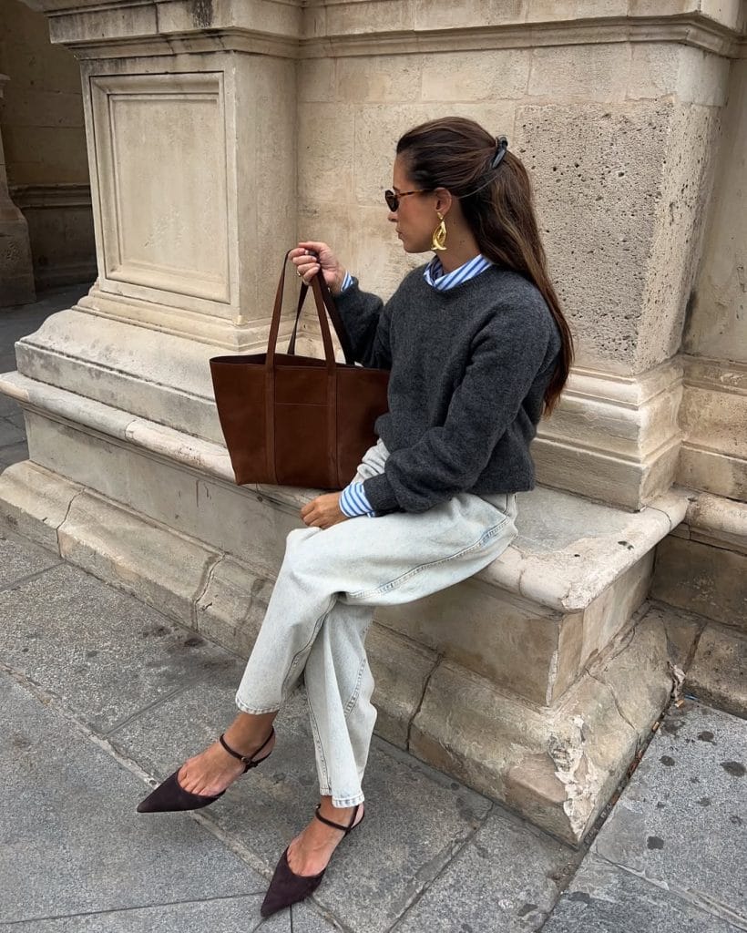 Casual fall work outfit with gray sweater, striped shirt, light wash jeans, brown tote bag and black flats