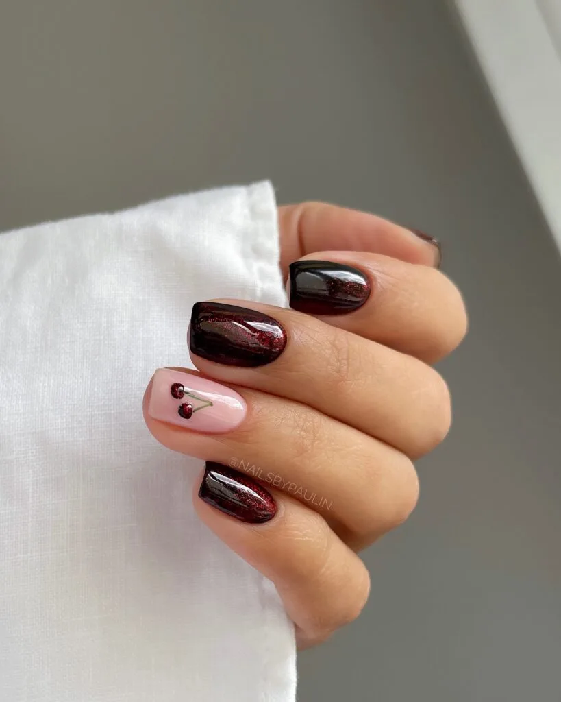 Dark red shimmer fall nails with one pale pink accent nail featuring tiny cherry nail art.