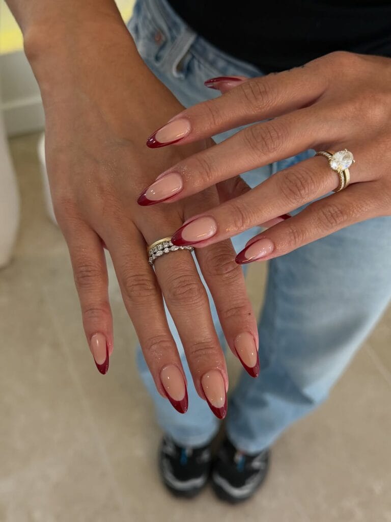 Glossy almond fall French tip nails with sheer nude bases and deep burgundy tips.