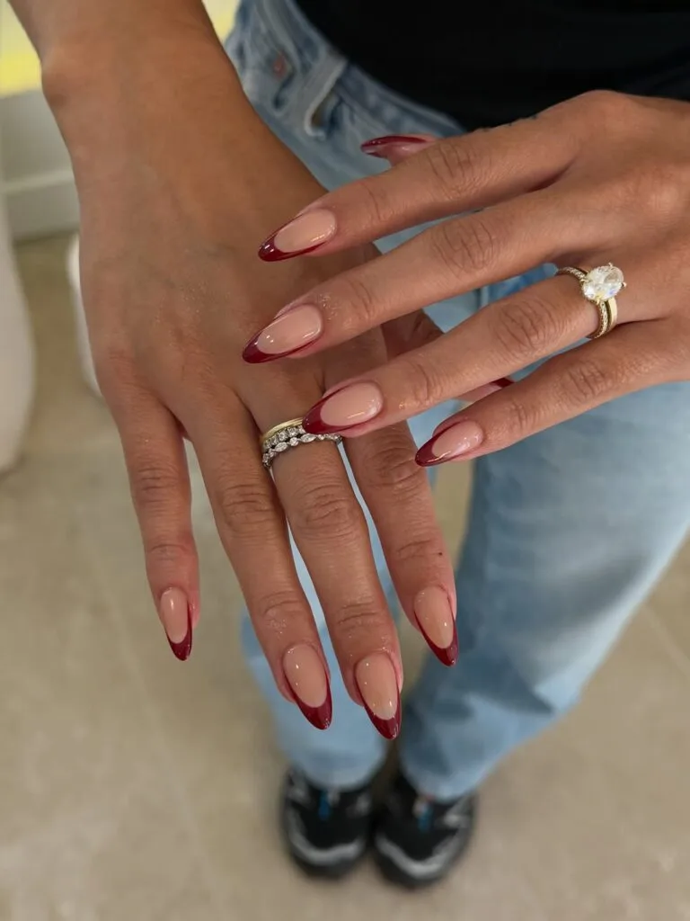 Glossy almond fall French tip nails with sheer nude bases and deep burgundy tips.

