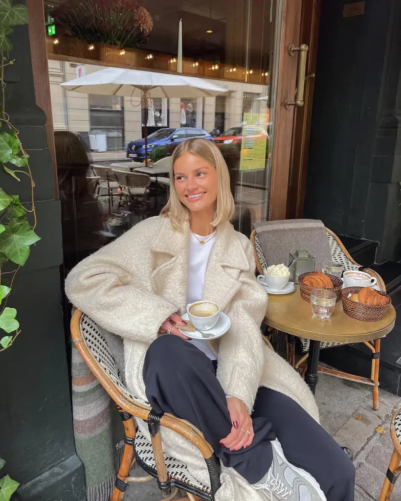 Cozy fall outfit with long cream teddy coat over white tee and navy trousers, finished with chunky sneakers