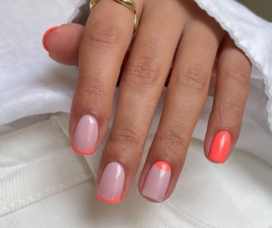 Short summer nails with milky base featuring coral French tips, half-moon design, and solid coral accent