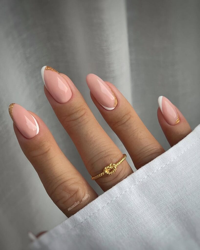  neutral nails with white French tips and gold glitter cuticle accents on nude pink almond shape
