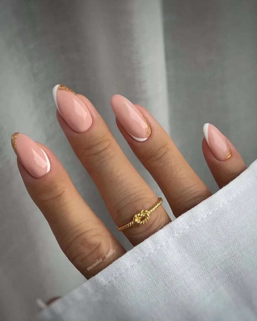 neutral nails with white French tips and gold glitter cuticle accents on nude pink almond shape