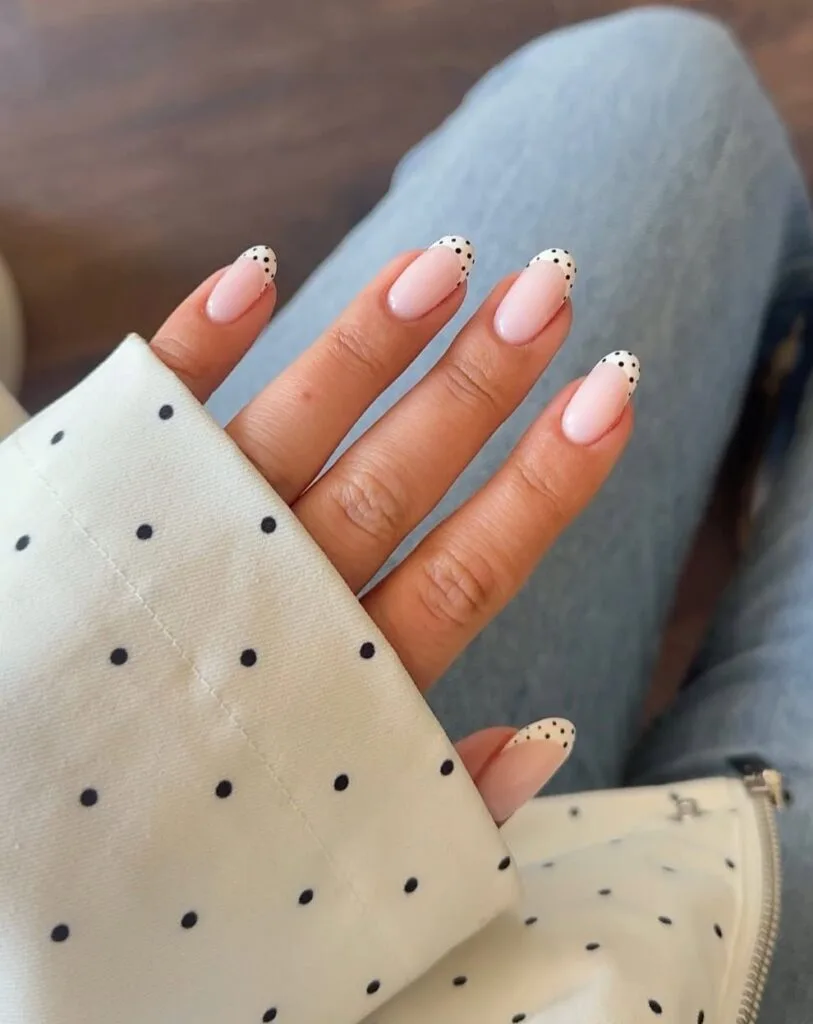 neutral nails with scattered black polka dot French tips on nude pink oval shape