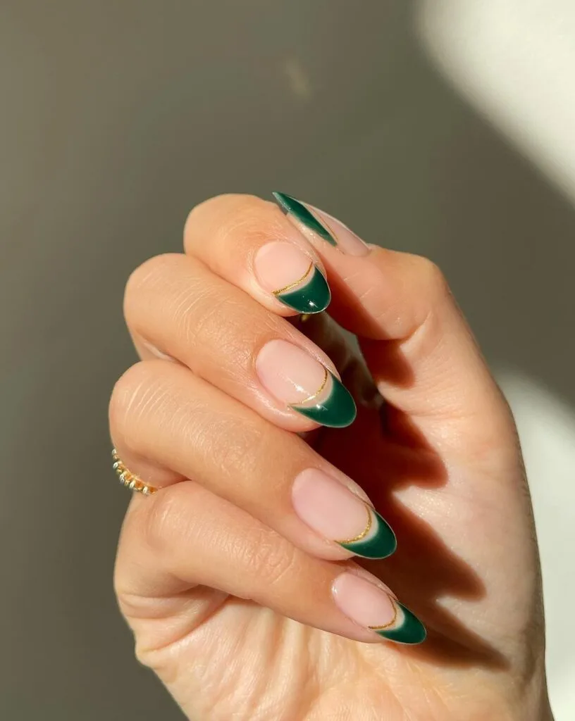 Nude nails with dark green French tips and thin gold line accents