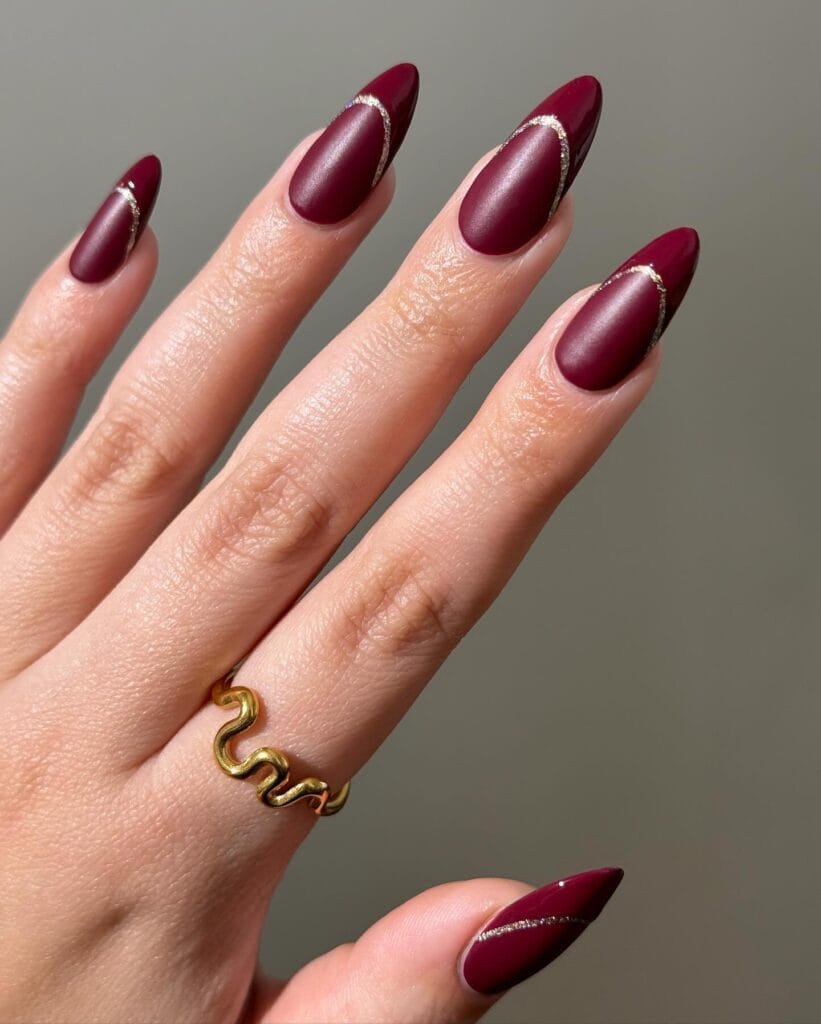 Matte burgundy almond nails with glossy tips and silver arc accents