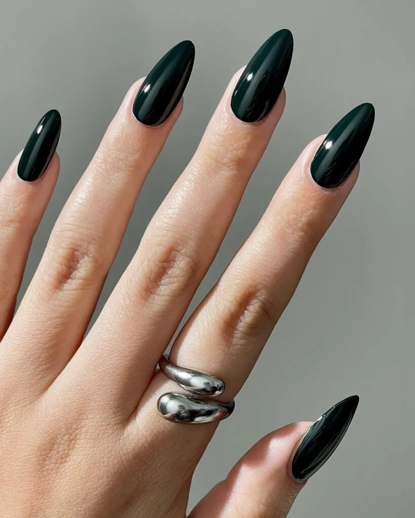 Long almond nails painted in glossy near-black green polish