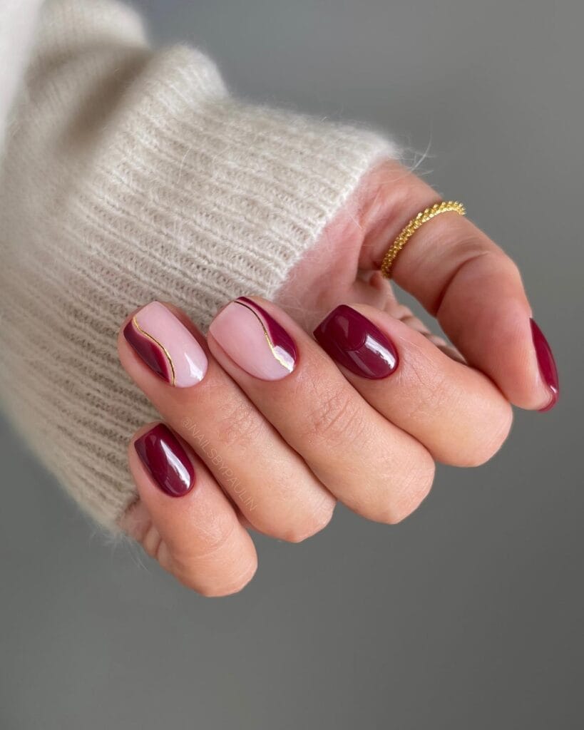 Burgundy and blush nails with gold wave accent lines