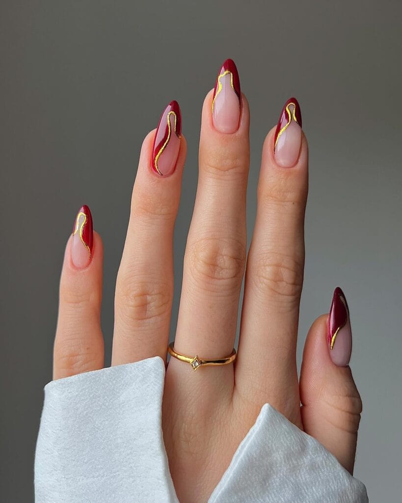 Burgundy French tip nails with gold swirl accents