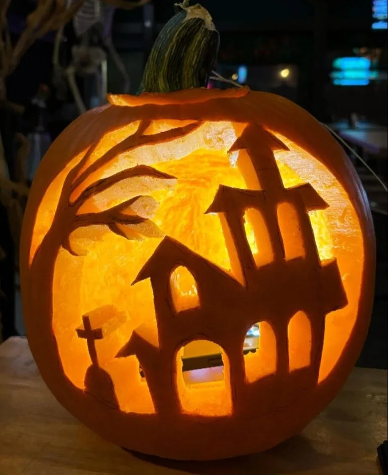 Pumpkin carving of haunted house scene with trees and glowing windows.