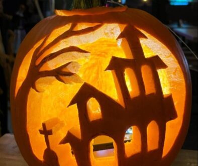 Pumpkin carving of haunted house scene with trees and glowing windows.