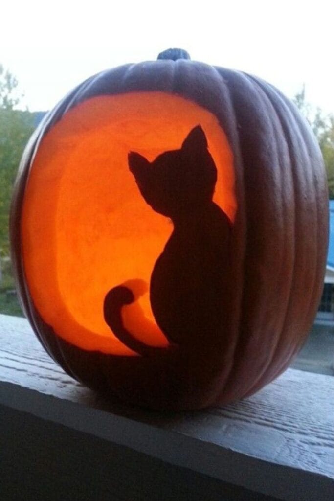 Pumpkin carving of cat silhouette against glowing round background.