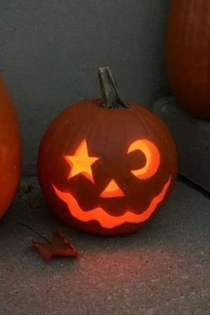 Pumpkin carving with star, moon, and triangle nose glowing.