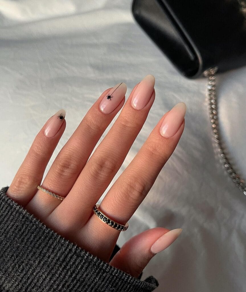 sheer nude almond nails with two tiny black spider accents, minimal Halloween nail idea
