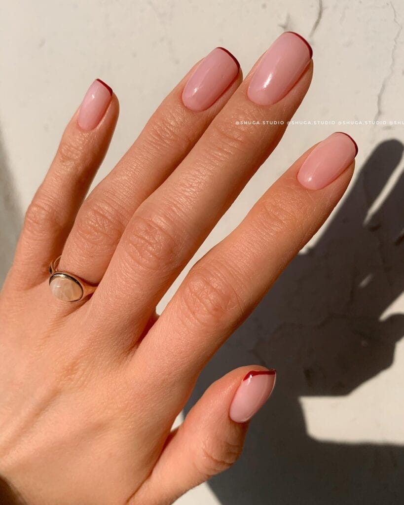 short square nails with sheer pink base and thin red French tips, October nail ideas