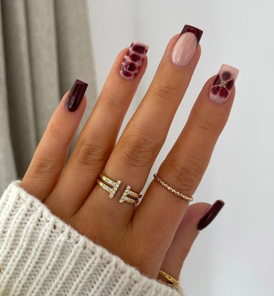 Burgundy snake print nails with nude base and floral accent with gold gems