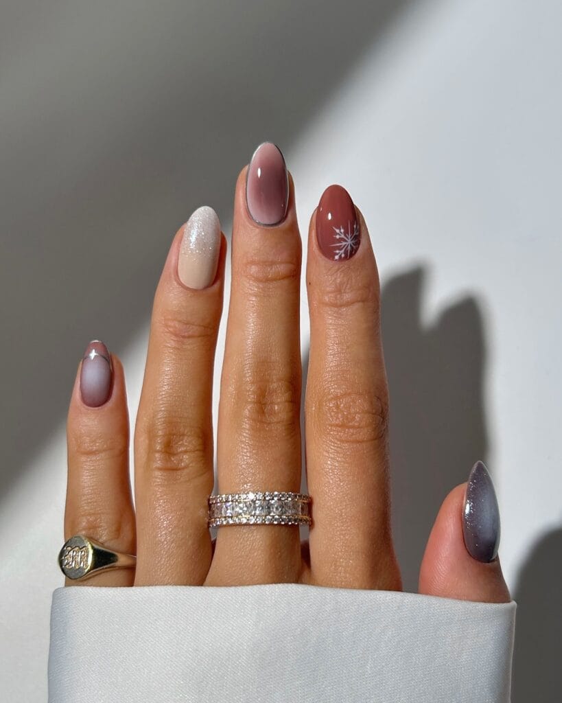 January nails with mixed neutral and smoky tips, glitter accent, and a white snowflake on rust polish.
