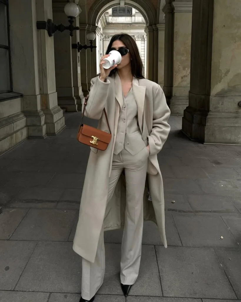 winter work outfit with beige long coat, matching vest and trousers, neutral top, brown shoulder bag, pointed heels
