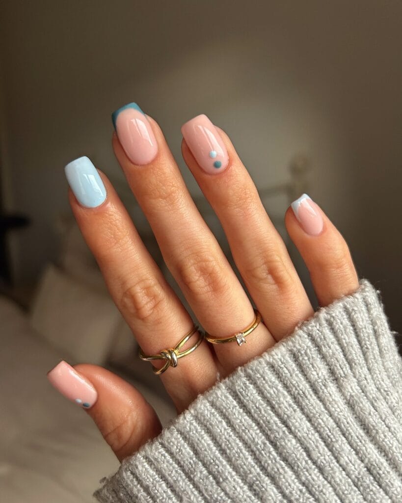 January nails with nude base, pastel blue tips, and tiny blue dot accents on short square nails.
