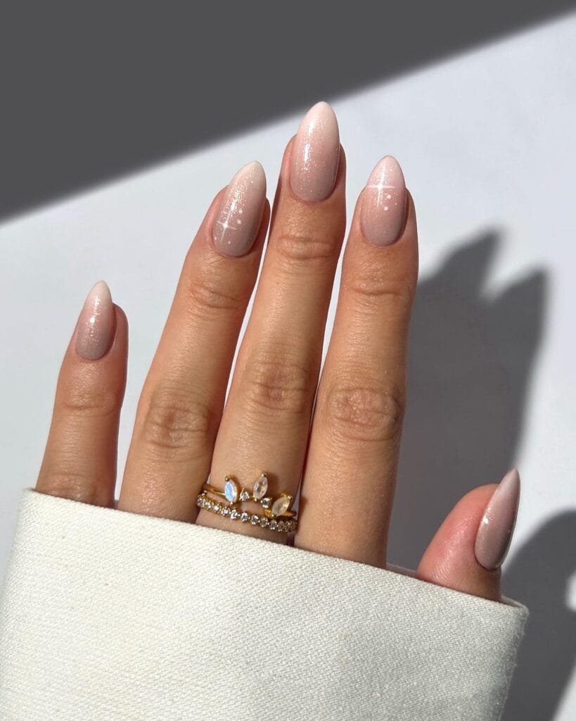 January nails in sheer taupe shimmer with tiny white starburst details on almond nails.
