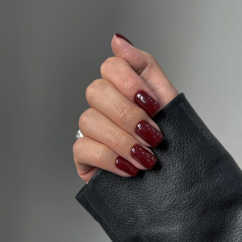 short winter nails in deep wine red, glossy finish, square shape, black leather clutch