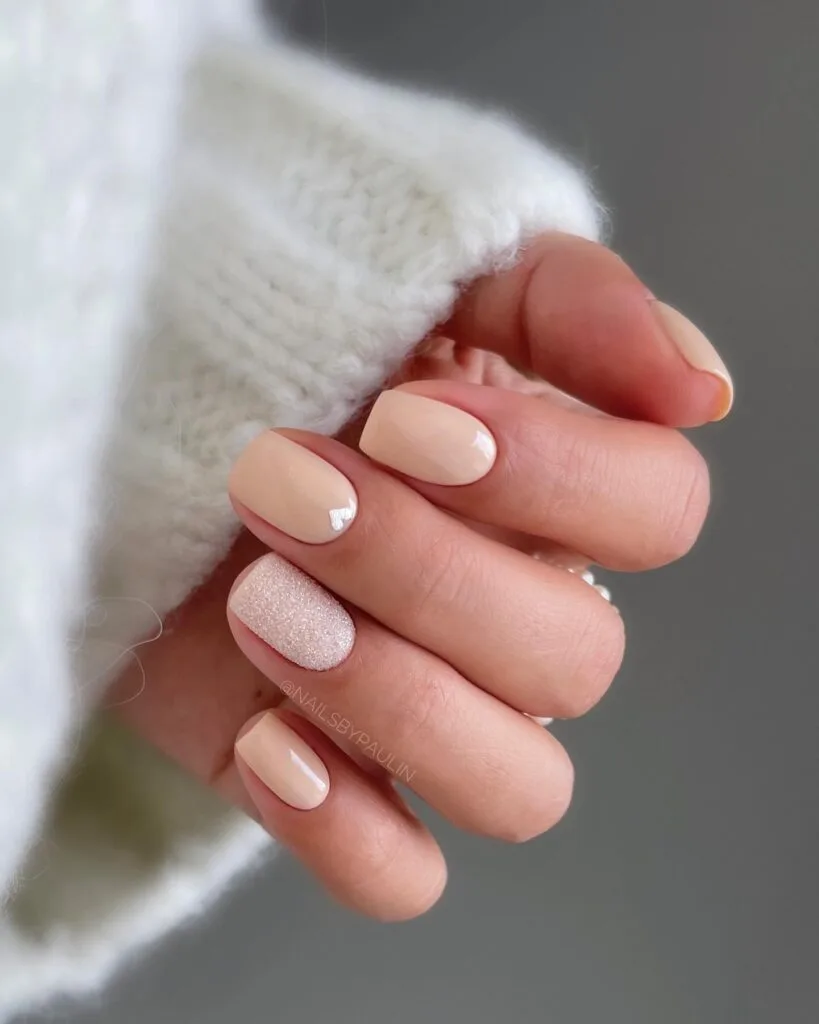 beige nude nails, one glitter accent, and tiny heart detail; simple winter nails.