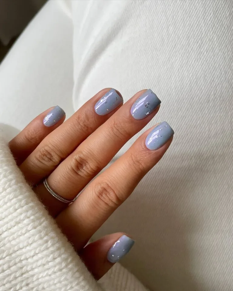 January nails in periwinkle blue with scattered silver foil flakes on short square nails.
