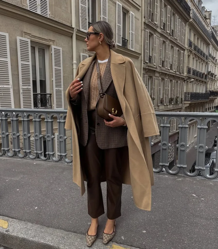 winter work outfit with camel coat, patterned blazer, beige sweater, brown leather trousers, brown handbag, flats
