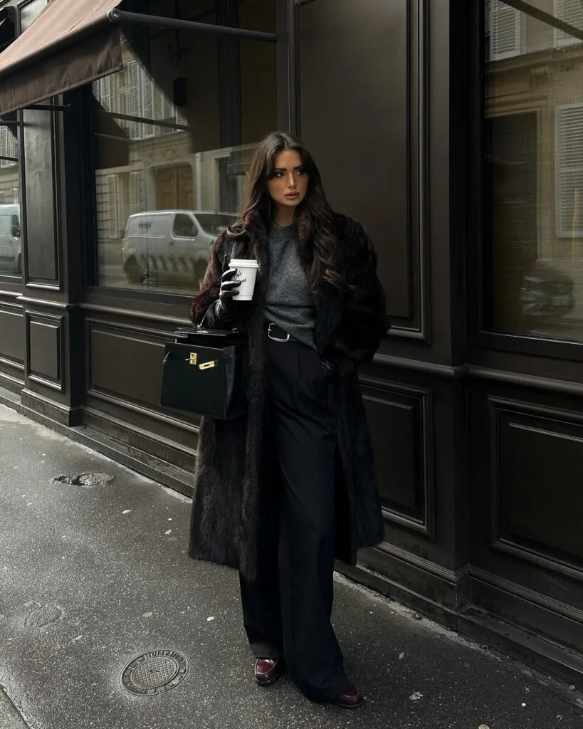 woman wearing black faux fur coat, grey sweater, black trousers, black gloves, black bag, chic winter outfit