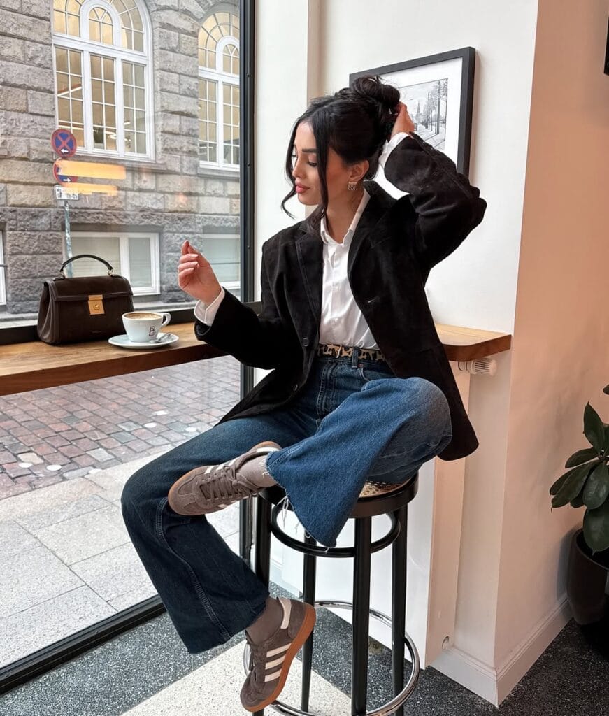 Woman in black blazer and white shirt with wide-leg jeans and sneakers, casual winter work outfit.

