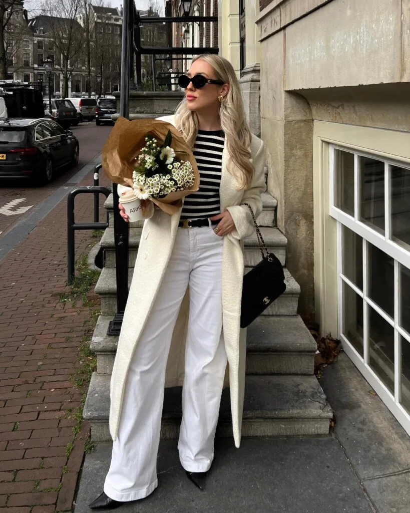 Cream coat with striped top and white trousers, black pointed boots, and chain bag—chic casual winter outfits.
