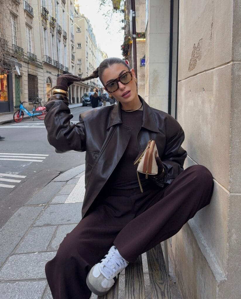 Woman in relaxed dark brown leather jacket and wide pants, chocolate brown trend, city street style.