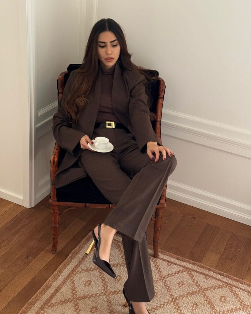 Model in tailored chocolate brown suit and turtleneck, chocolate brown trend, sitting indoors with heels.