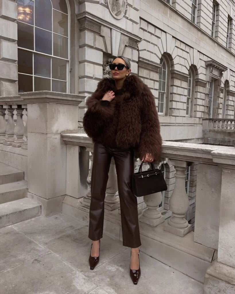 Woman in chocolate brown fur coat and leather pants, chocolate brown trend, city backdrop and sunglasses.
