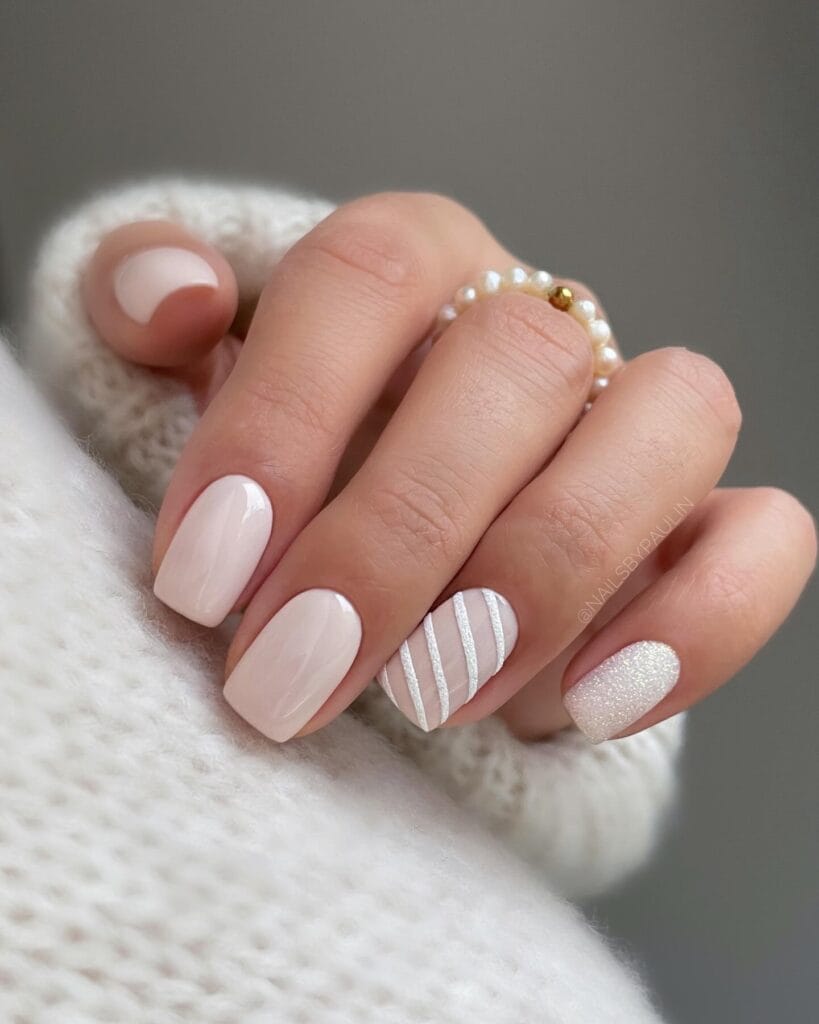 Soft milky nude January nails with silver striped accent and a sugar-glitter white nail on short squares.
