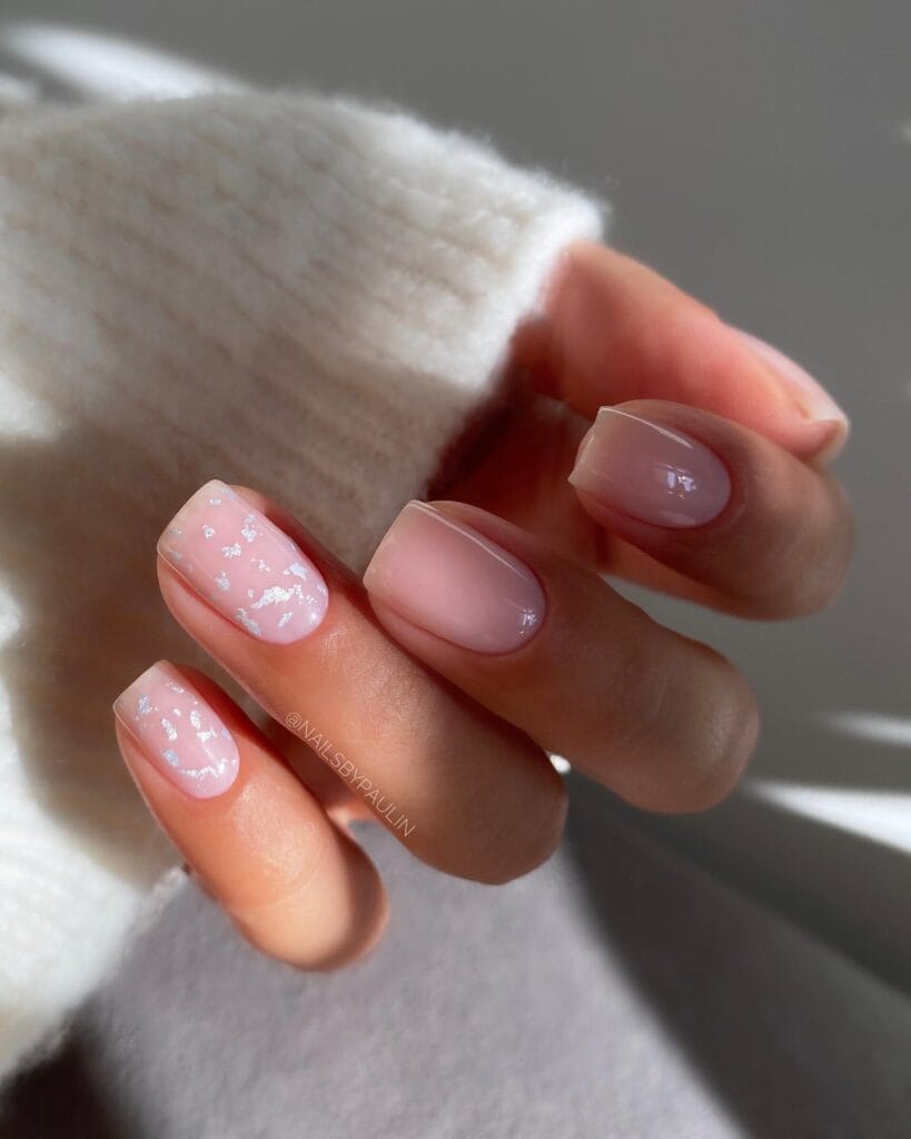 Sheer pink January nails with scattered silver foil flakes on short rounded nails.
