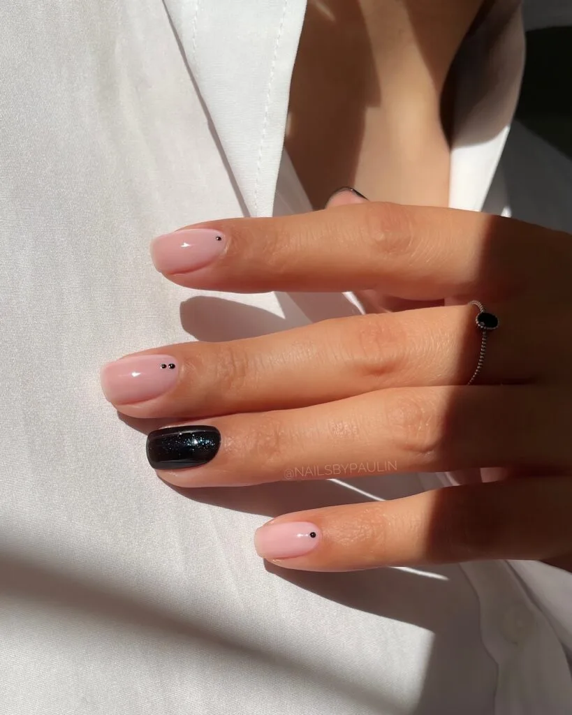Blush pink manicure with tiny black dot accents and one black glitter statement nail, simple winter nails.