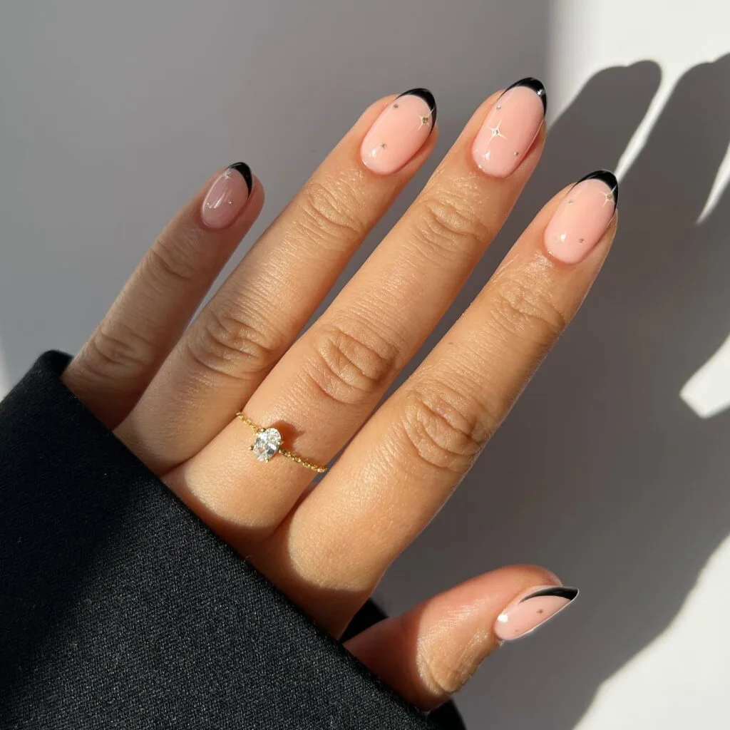 Nude manicure with micro black French tips and tiny star accents, simple winter nails.