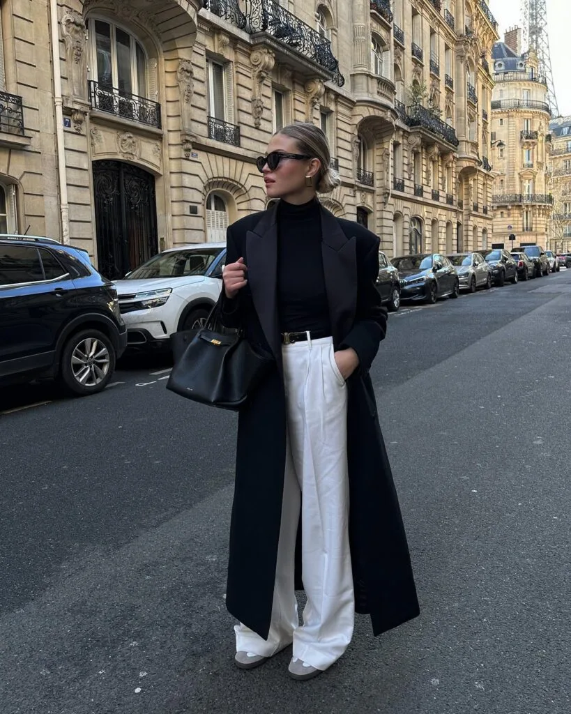 woman in black coat , black turtleneck, white trousers, carrying black tote, winter city outfit