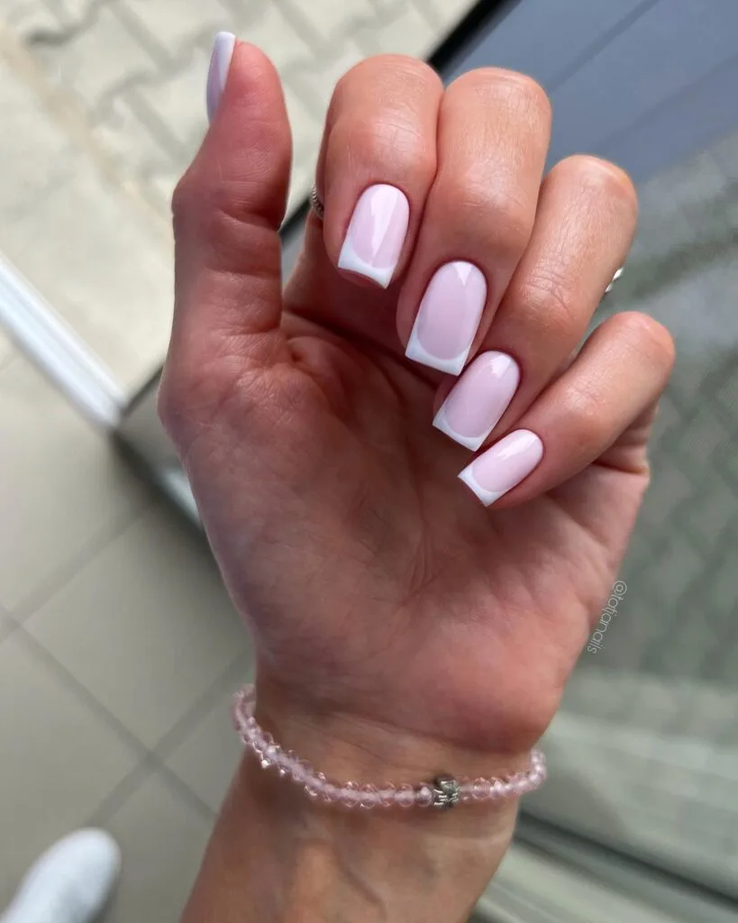Simple winter nails with pale pink base and crisp white French tips on short square nails.