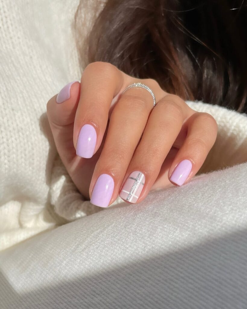 Glossy lilac January nails with a nude accent featuring thin silver-and-white plaid lines on short squares.
