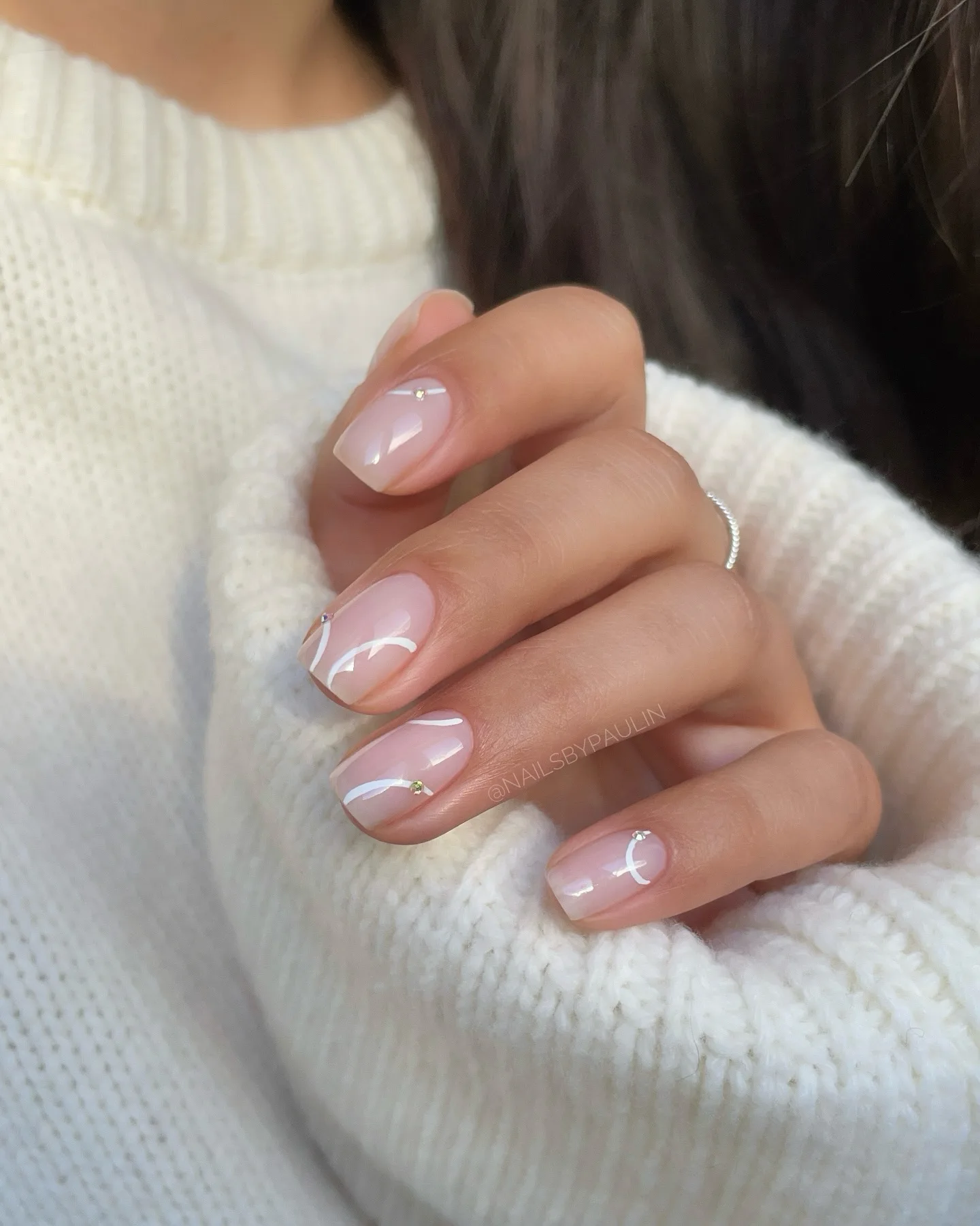 milky pink winter nails with white curved lines and tiny silver studs