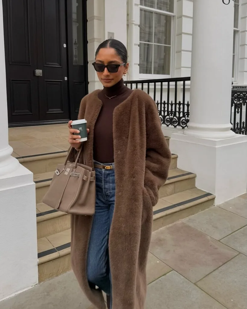 Alt text: woman in chocolate faux fur coat, jeans, taupe Birkin bag, sunglasses, winter cozy chic look