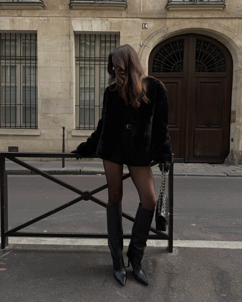 Black faux fur jacket with black knee-high boots, Statement-Making Long Boots trend, city street, all-black look.